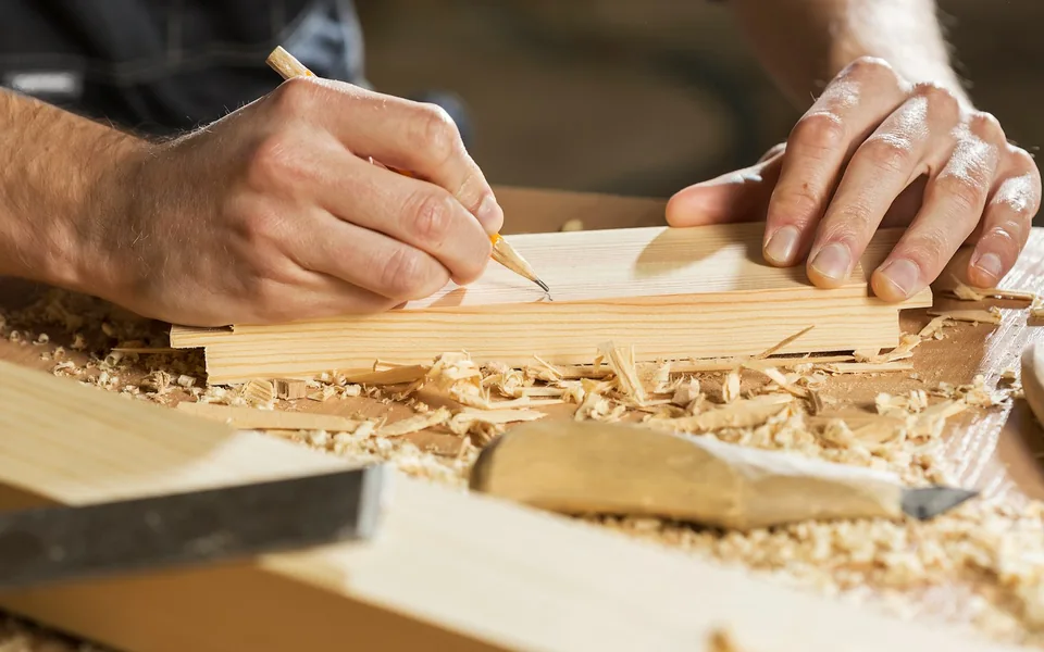 Woodworker marking a timber board beside wood shavings.